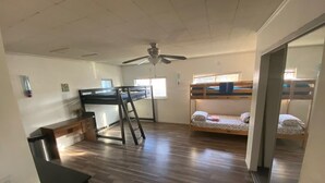 A room with a bunk bed, a desk with a chair, a ceiling fan, and a window.