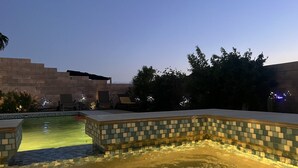 En swimmingpool med ett kaklat poolområde, omgiven av en låg mur av tegelsten och träd.
