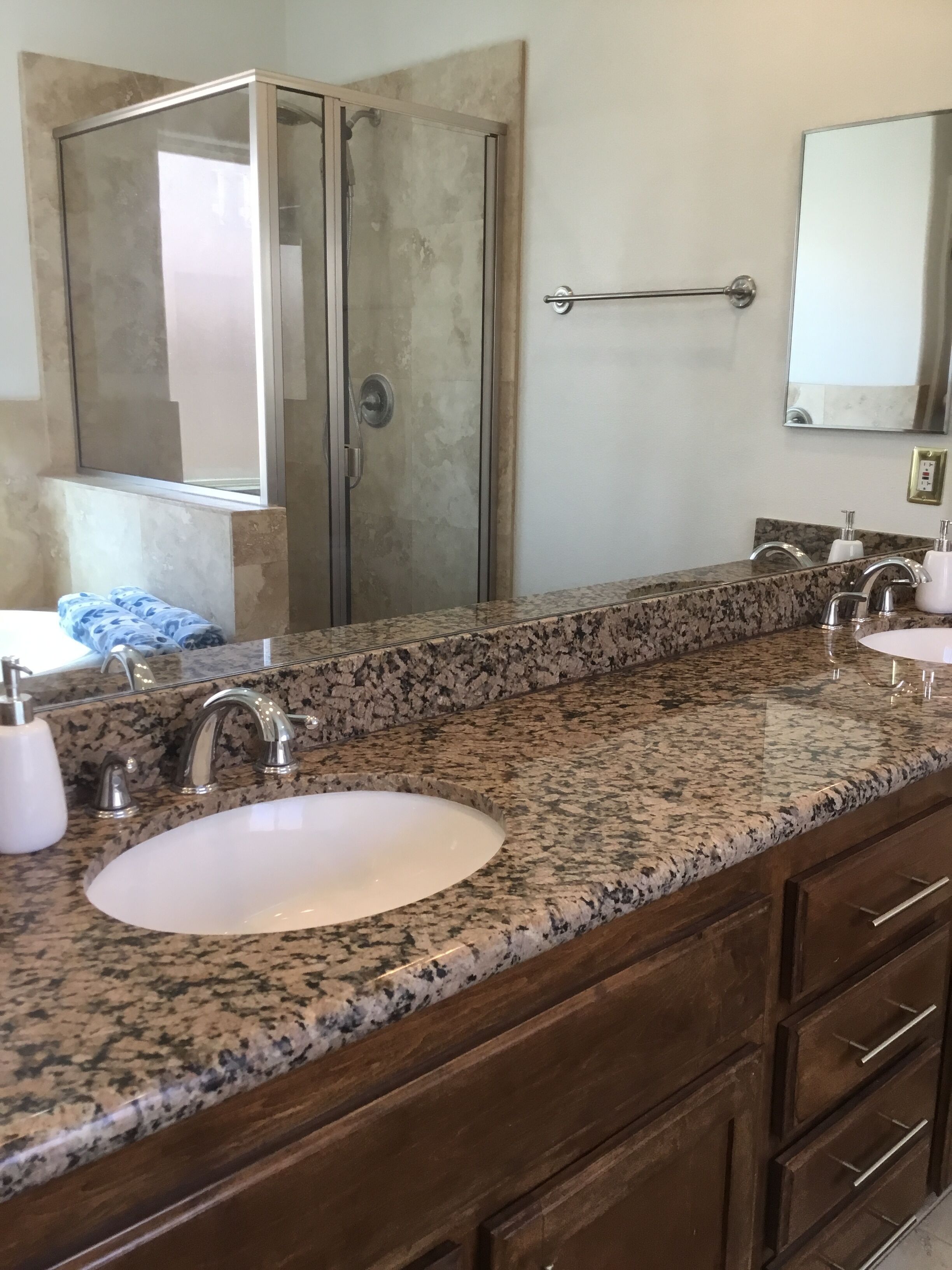 Une salle de bain avec un comptoir en granit, deux lavabos, une douche et un miroir.
