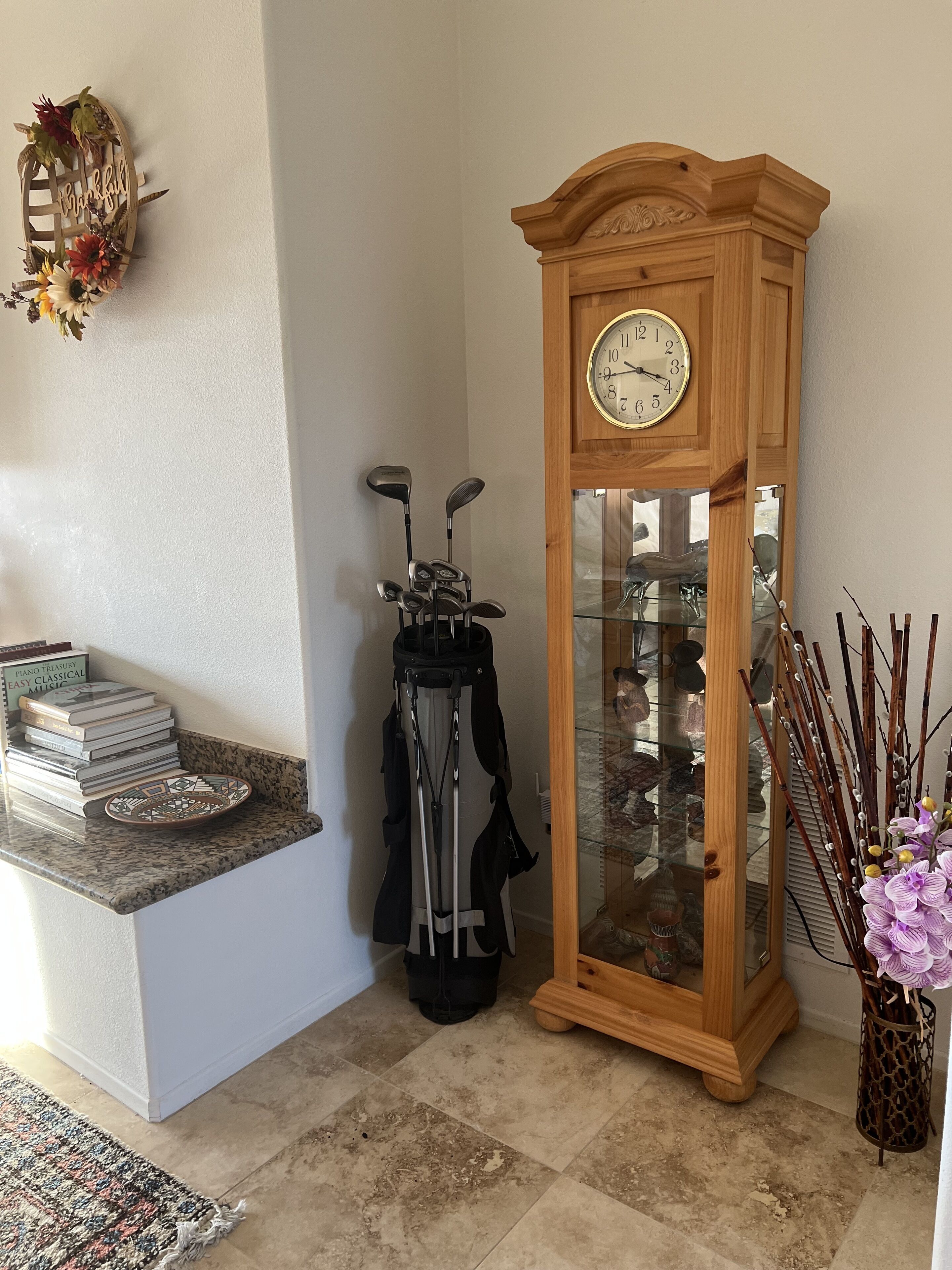 Una esquina de una habitación con un reloj de madera, un bolso de golf y un jarrón con flores.