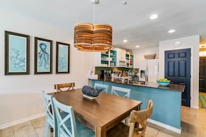 Une cuisine moderne avec un îlot central bleu, des armoires blanches et une table à manger en bois avec des chaises.