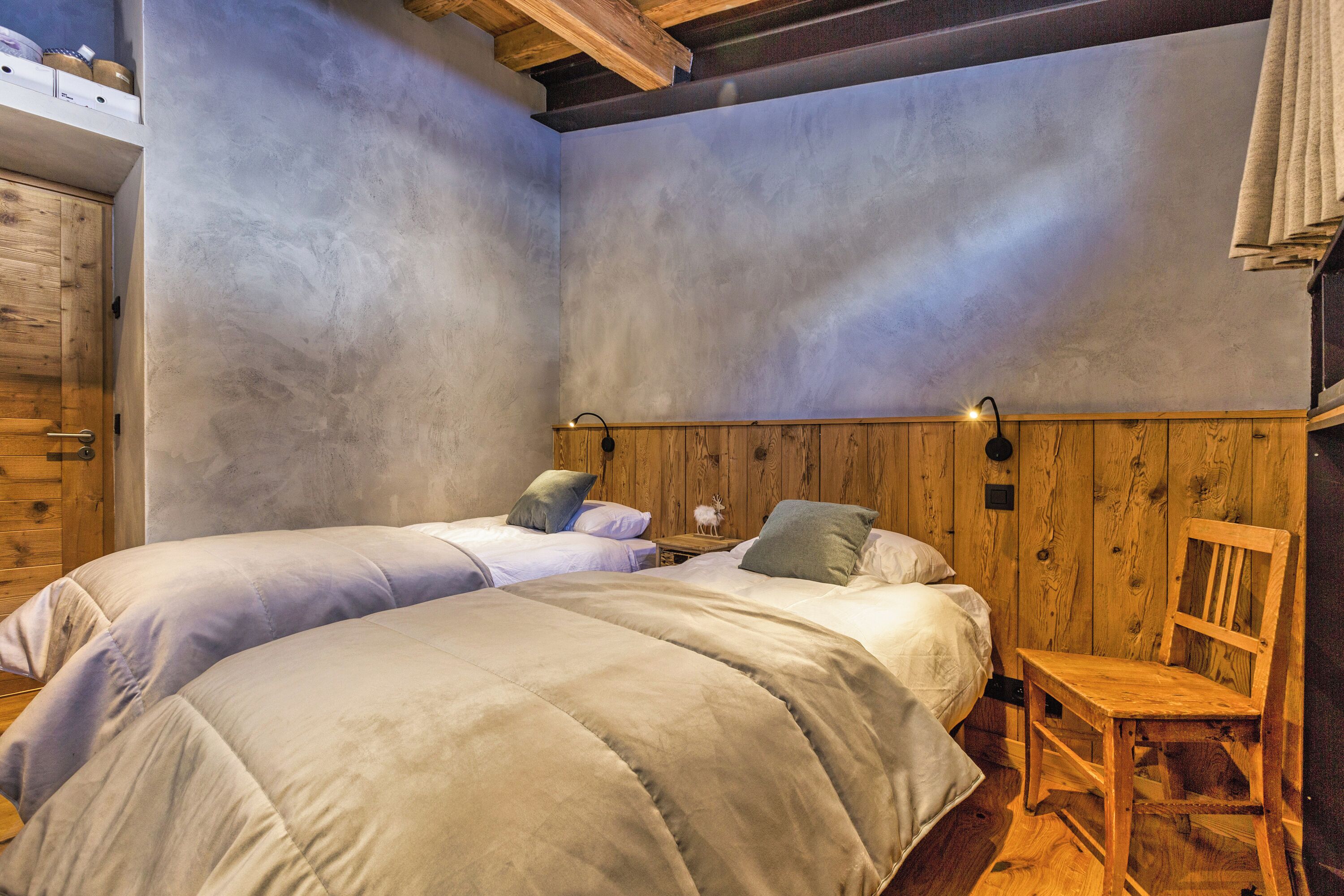 A room with two beds, wooden walls, and a wooden chair.
