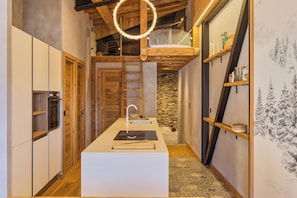 Une cuisine étroite dotée d’un îlot central, de meubles en bois, d’un mur en pierre et d’un luminaire suspendu.