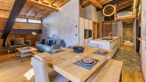 Ein modernes Loft mit freiliegenden Holzbalken, einem Essbereich mit großem Tisch für vier Personen und einem gemütlichen Wohnbereich mit Sofa und Kamin.