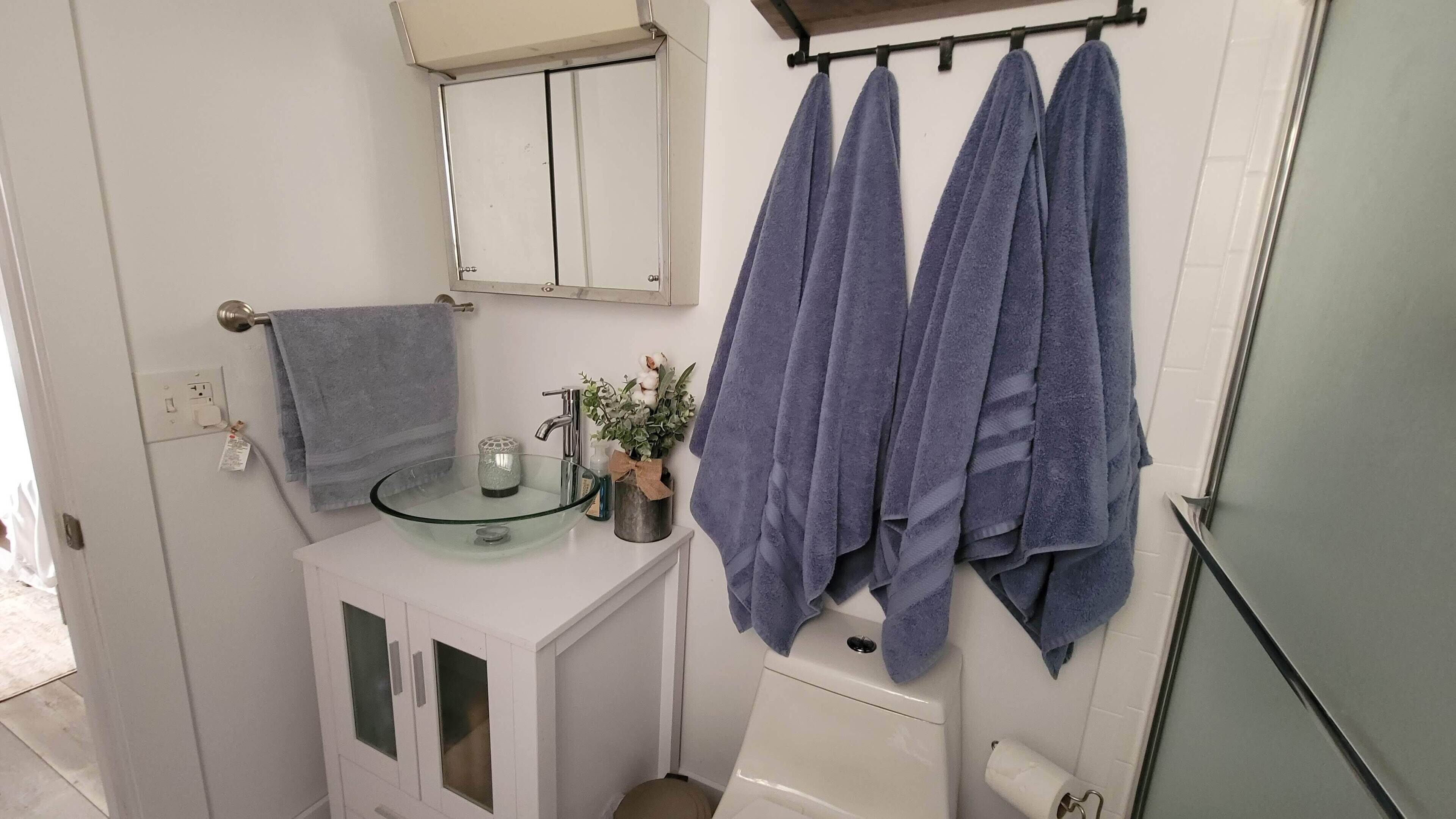 Un baño con un lavabo de cristal, un armario blanco, un espejo y dos toallas colgadas en un perchero.