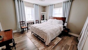 A bedroom with a large bed, wooden floor, two chairs, a desk, and a mirror. - No closer lodging to Crystal Bridges exists! (Bentonville)