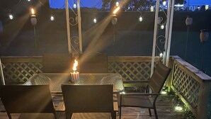 An outdoor wooden deck with a glass table and chairs, string lights, and a candle. - No closer lodging to Crystal Bridges exists! (Bentonville)