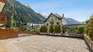 A courtyard with a tiled floor, a wooden fence, and a building with a balcony. - Duplex Aiguille du midi large terrasse, Chamonix, France (Chamonix)