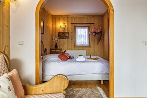 Ein gemütliches Schlafzimmer mit Holzvertäfelung, einem Bett mit weißer Bettwäsche, einem Nachttisch mit Blumen in einer Vase und einem Fenster mit Spitzenvorhängen.