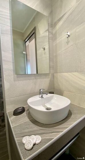 Un baño con un lavamanos redondo, un espejo y un toallero.