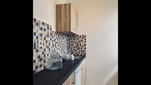 Una cucina con un piano di lavoro nero, un armadietto in legno, uno schienale piastrellato e un lampadario.
