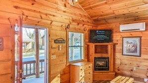 L’intérieur d’un chalet en bois chaleureux et accueillant, avec une cheminée, un téléviseur fixé au mur et une porte donnant sur l’extérieur.