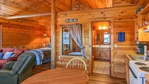 Un intérieur de chalet chaleureux avec une table à manger en bois, un canapé, un lit et un coin cuisine.