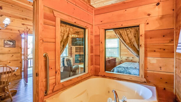 L’intérieur d’un chalet en bois comprend une grande baignoire en bois, une table à manger avec des chaises et une fenêtre avec des rideaux.