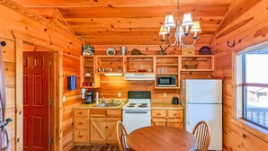 Une cuisine rustique aménagée dans une cabane en bois, avec une table à manger, des chaises, un poêle, un réfrigérateur, un four à micro-ondes et un lustre.