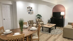 A modern living room with a dining area, featuring a wooden dining table, chairs, a sofa, a TV, and a coffee table. - Lakeside Suite - Two bed, Two bath Suite in Nelson  (Nelson)