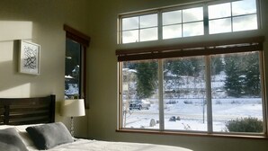 A bedroom with a large window, a bed with pillows, a bedside table, and a wall-mounted lamp. - Lakeside Suite - Two bed, Two bath Suite in Nelson  (Nelson)