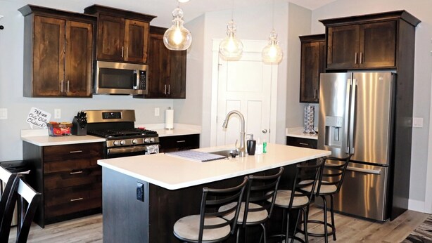 A modern kitchen with dark wooden cabinets, stainless steel appliances, and a central island with bar stools. - Chitty Chitty Chubbuck 🎶 We love you! ❤️  Arcade! Ping Pong!  (Chubbuck)