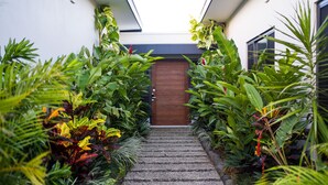 Una escalera que lleva a una puerta de madera, rodeada de exuberante vegetación tropical.