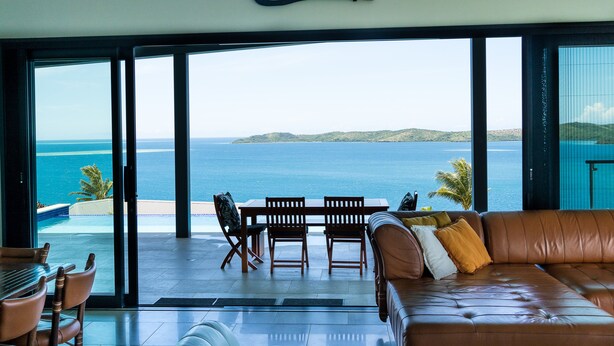 Un salón moderno con un amplio ventanal de vidrio que da a una piscina y vistas al océano.