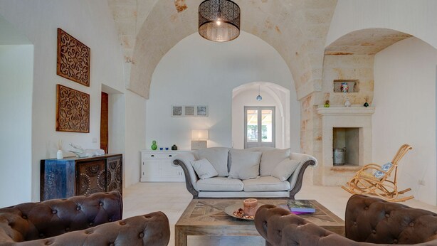 A spacious living room with a high arched ceiling, a fireplace, and a view through an archway to a kitchen.