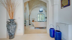 An interior hallway with a rustic stone archway leading to a bedroom. A large decorative vase and two blue vases are placed on the floor.