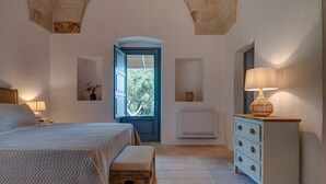 A bedroom with a bed, bedside table, lamp, dresser, and a view through an open door.