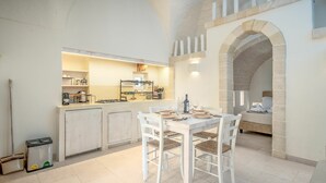 A modern kitchen with white cabinetry, a dining table set for four, and a stone archway leading to a bedroom. - Villa in Ostuni with 1 bedrooms sleeps 2 (Ostuni)