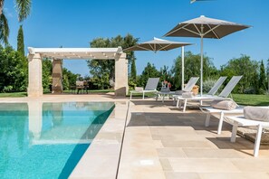 A swimming pool with lounge chairs and umbrellas, surrounded by greenery.