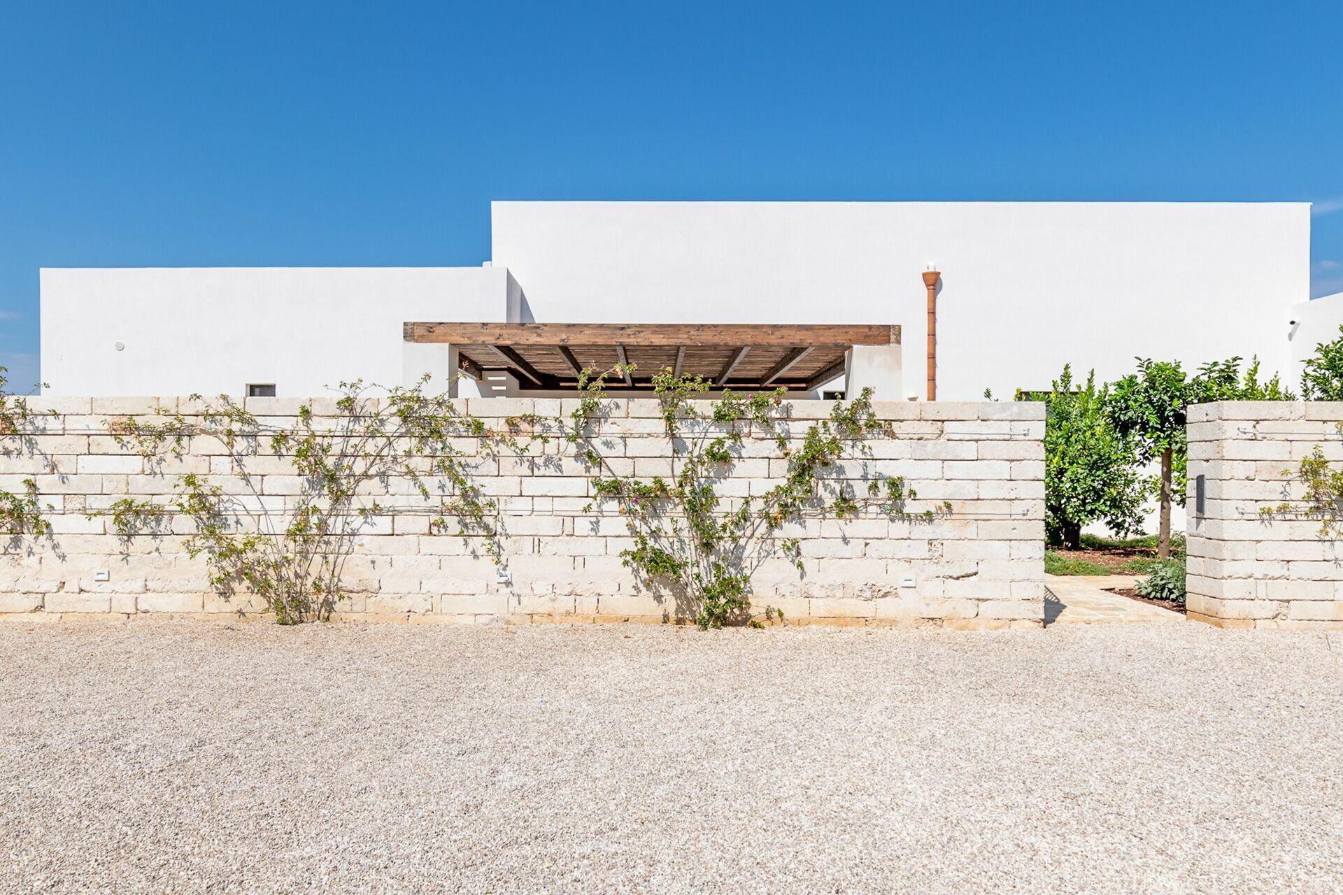 A modern building with a white facade, a wooden pergola, and a gravel driveway.