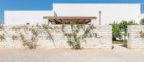 A modern building with a white facade, a wooden pergola, and a gravel driveway.