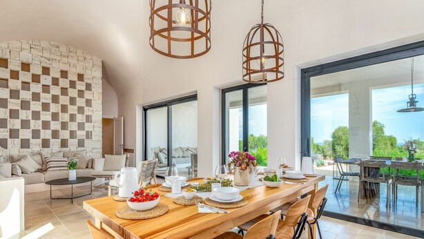 A spacious dining area with a wooden table set for a meal, large windows offering a view of the outdoors, and a modern living space with a checkered wall and comfortable seating. - Villa in Ostuni with 6 bedrooms sleeps 11 (Ostuni)