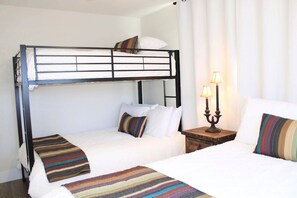 Cozy accommodations feature a bunk bed and a single bed, each with a comfortable mattress and pillows, along with a nightstand and lamp.