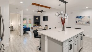 A modern kitchen with a white island, black chairs, and a dining area with a blue chair. - Beautiful Fully Remodeled Home (Austin)