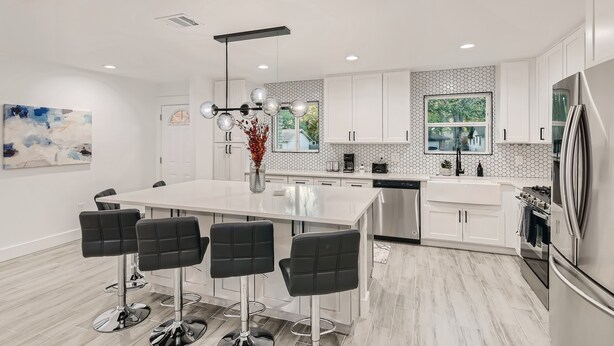 A modern kitchen with a central island, bar stools, and stainless steel appliances. - Beautiful Fully Remodeled Home (Austin)