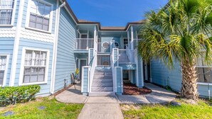 A two-story house with a front porch, a staircase, and a palm tree.