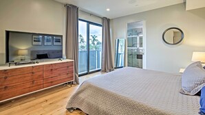 A bedroom with a large bed, a dresser, a TV, and a balcony with curtains.