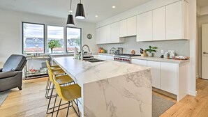 A modern kitchen with a marble island, white cabinets, and a large window offering a view of the neighborhood.