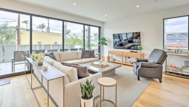 A modern living room with a sofa, coffee table, and TV. There is a balcony with a table and chairs.