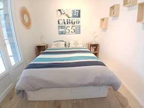 Quarto com cama, janela, relógio de parede, quadro emoldurado e prateleira pequena.