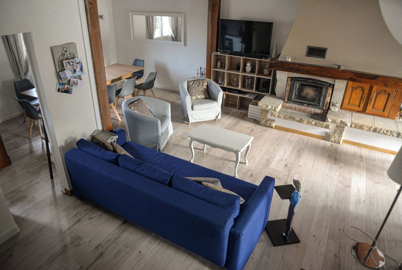 A living room with a blue sofa, a wooden dining table, and a TV mounted on the wall.