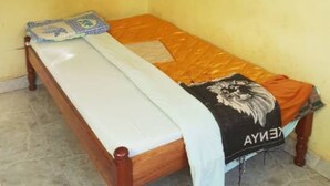A single bed with a white mattress and an orange blanket, a mosquito net above, and a blue pillow on the left side. - Jaybee's Resort (Eldoret)