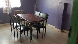 A dining area with a table and chairs, a window with curtains, and a green door. - Jaybee's Resort (Eldoret)