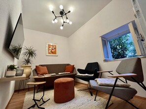 Un salon moderne comprenant un canapé, deux fauteuils, une petite table, un miroir, une plante en pot et un luminaire suspendu au plafond.
