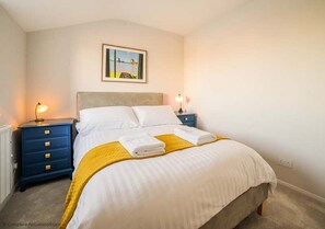 A neatly made bed with white and yellow bedding, two bedside tables with lamps, and a framed picture on the wall. - Rampart View -  a house that sleeps 6 guests  in 3 bedrooms (Gosport)