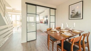 A modern dining area with a wooden table set for four, a kitchen in the background, and a staircase leading to another level. - Rampart View -  a house that sleeps 6 guests  in 3 bedrooms (Gosport)