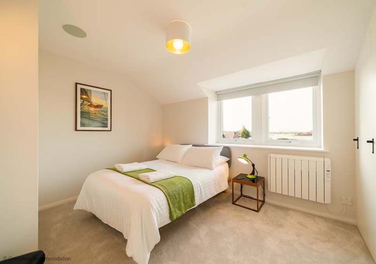 Un dormitorio con cama, ventana, radiador y un cuadro en la pared.