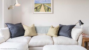 A living room with a white sofa, two black and beige pillows, a framed picture on the wall, and a floor lamp. - Rampart View -  a house that sleeps 6 guests  in 3 bedrooms (Gosport)