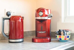 A red coffee maker and a kettle on a kitchen counter next to a window. - Rampart View -  a house that sleeps 6 guests  in 3 bedrooms (Gosport)