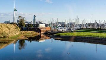 Una masa de agua tranquila que refleja edificios y un puente, con un paisaje urbano al fondo.